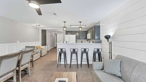 A modern kitchen with a central island, bar stools, and a dining area with a sofa and chairs.