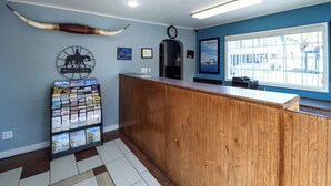 A reception area with a wooden counter, a welcome sign, a bulletin board with travel brochures, a clock, and a poster on the wall. - Hotel Inn Pendleton I-84 (Pendleton)