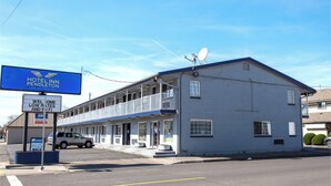A two-story motel with a balcony on the second floor, a satellite dish on the roof, and a signboard advertising low rates and a welcome message.
