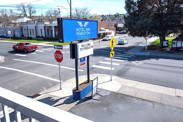 Une vue de rue avec une enseigne d’hôtel « Hotel Inn Pendleton », un panneau de signalisation indiquant un arrêt et un panneau de passage piéton.