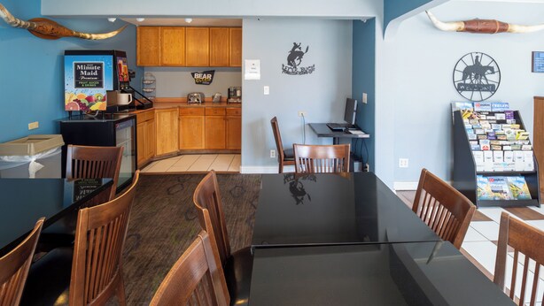 A modern kitchen with wooden cabinets, a coffee machine, and a dining area with a glass table and wooden chairs. - Hotel Inn Pendleton I-84 (Pendleton)