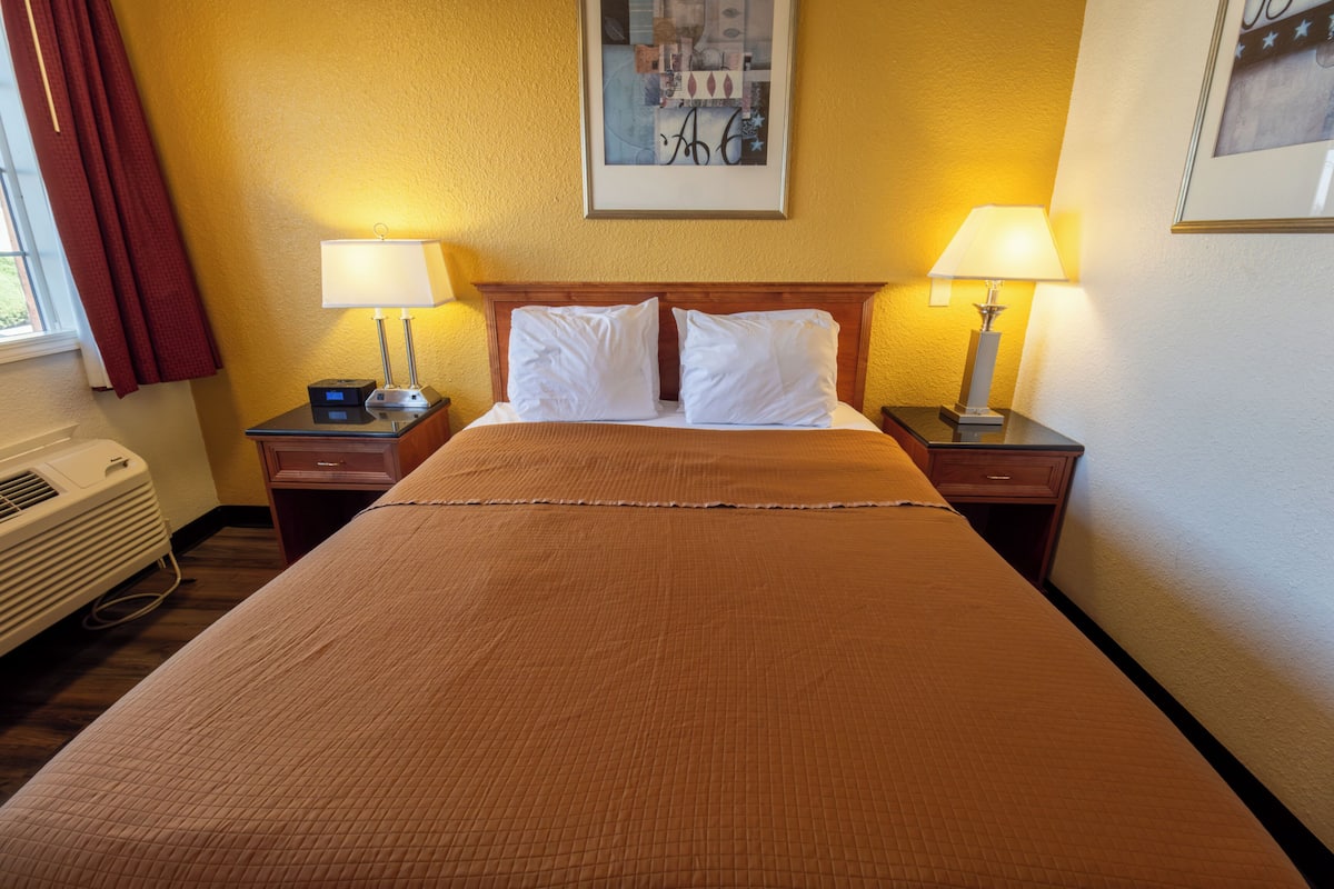 A hotel room with a large bed, two bedside tables with lamps, a heater, and a window with curtains.