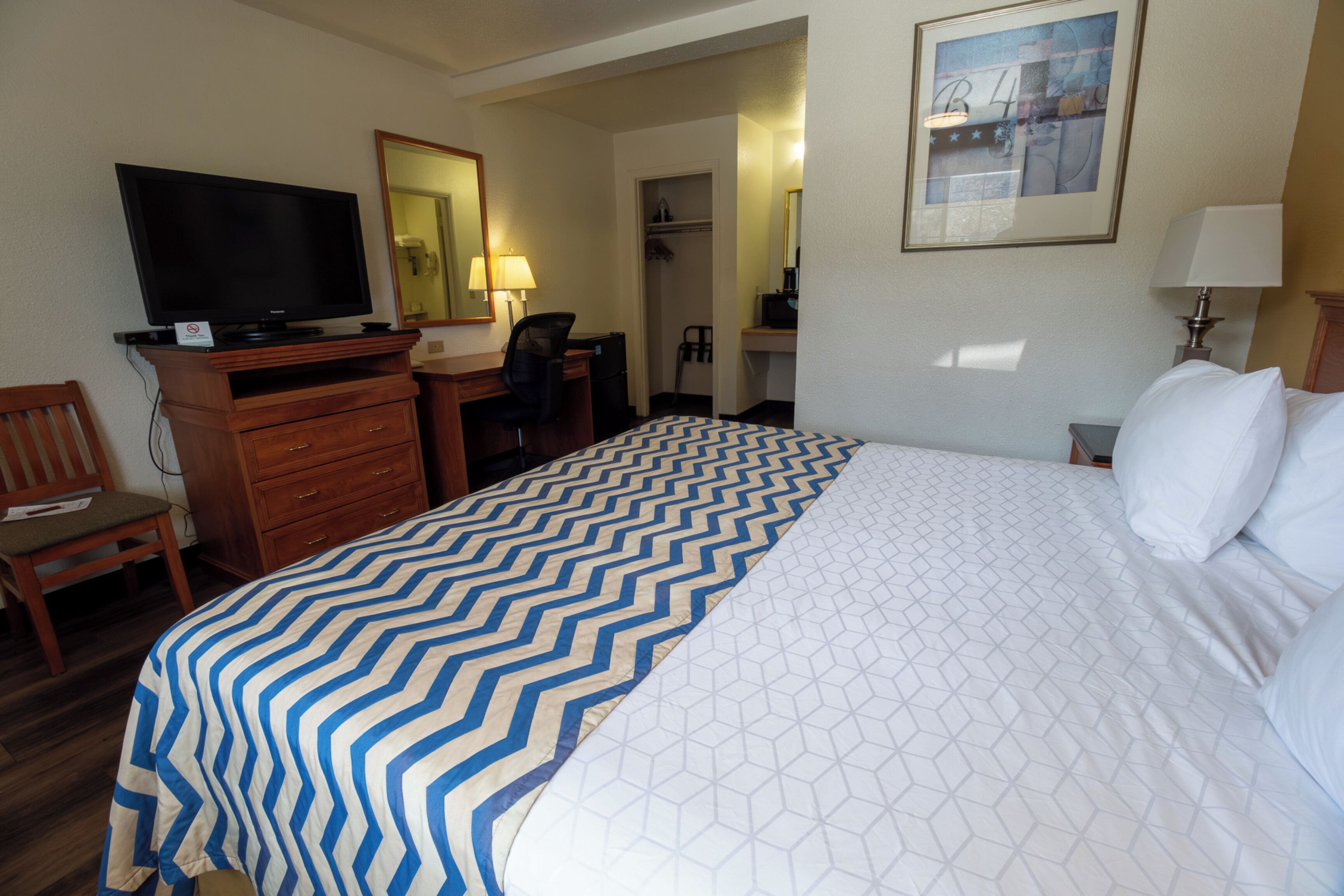 A hotel room with a large bed, a desk with a chair, a television, and a wardrobe.
