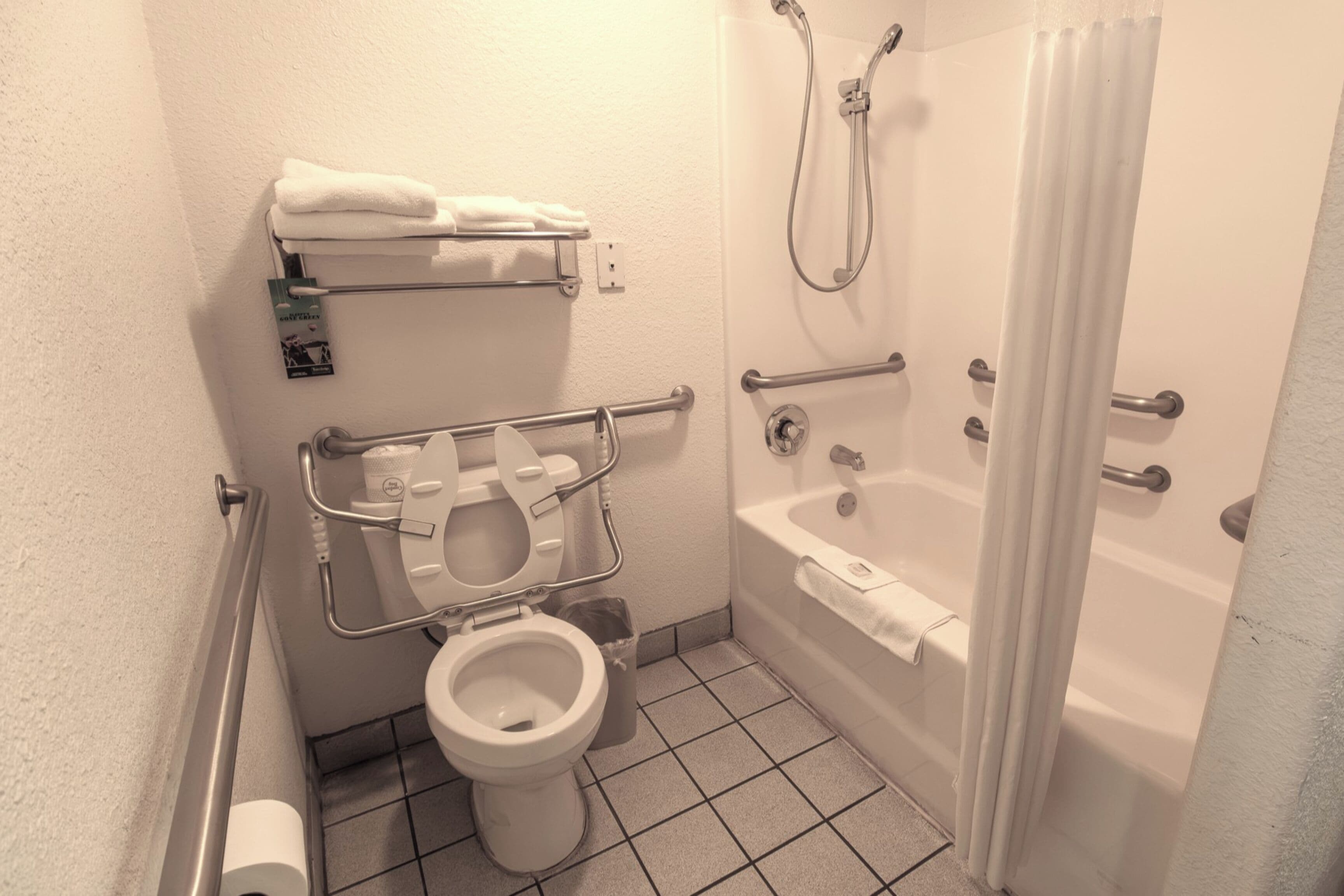 A bathroom with a toilet, grab bars, a shower, and a bathtub.