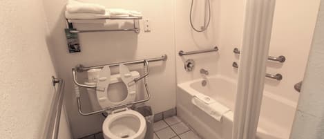 A bathroom with a toilet, grab bars, a shower, and a bathtub.
