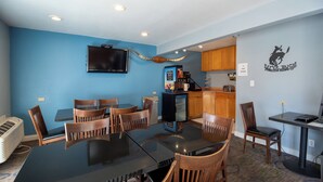 A dining area with a black glass table surrounded by wooden chairs, a coffee machine, and a television mounted on the wall.