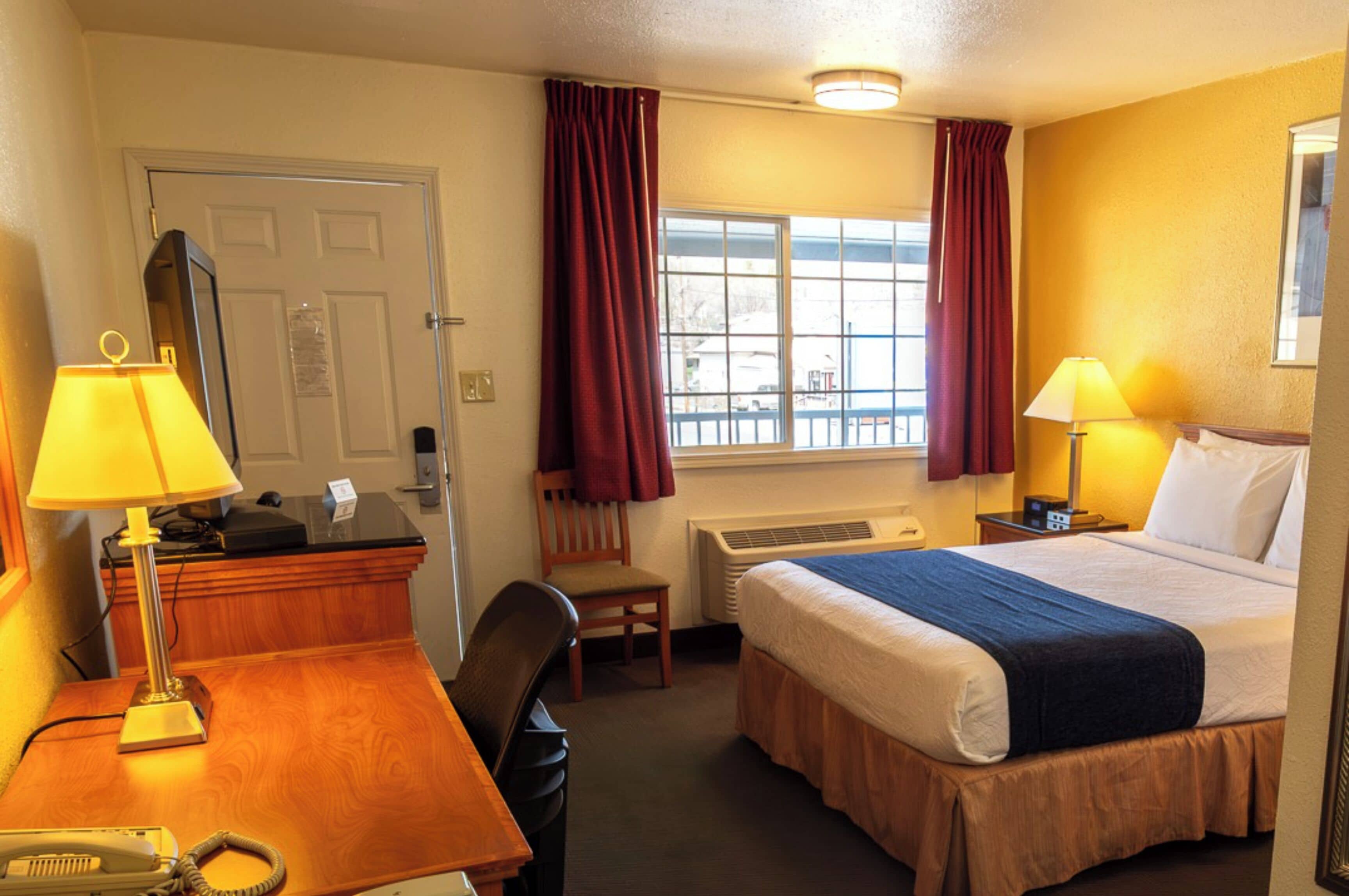 A hotel room with a bed, desk, chair, and two lamps.
