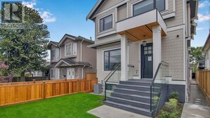 A two-story residential building with a front porch, a wooden fence, and a well-maintained lawn.