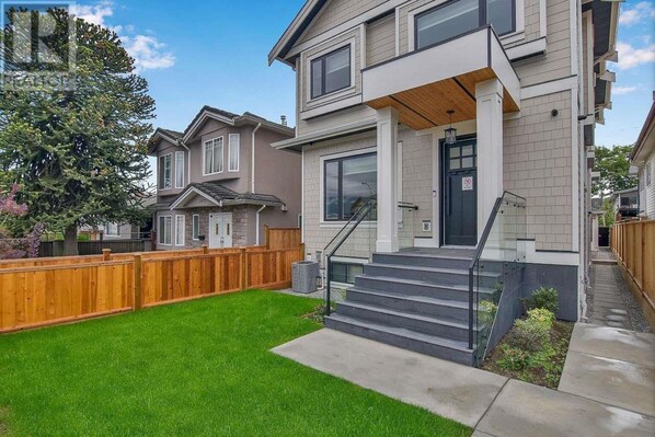 A two-story residential building with a front porch, a wooden fence, and a well-maintained lawn.