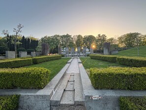 Un jardín formal con un camino central que lleva a un monumento, rodeado de setos y árboles cuidadosamente recortados.