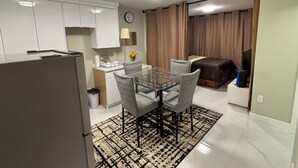 A compact living space with a kitchenette, a dining area with a glass table, and a separate sleeping area with a bed.