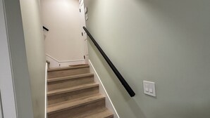 A staircase with wooden steps and a black handrail, leading to a landing with a white wall and a light switch.