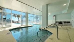 Piscina interior com paredes de vidro transparente, área de piscina e vista para o exterior.