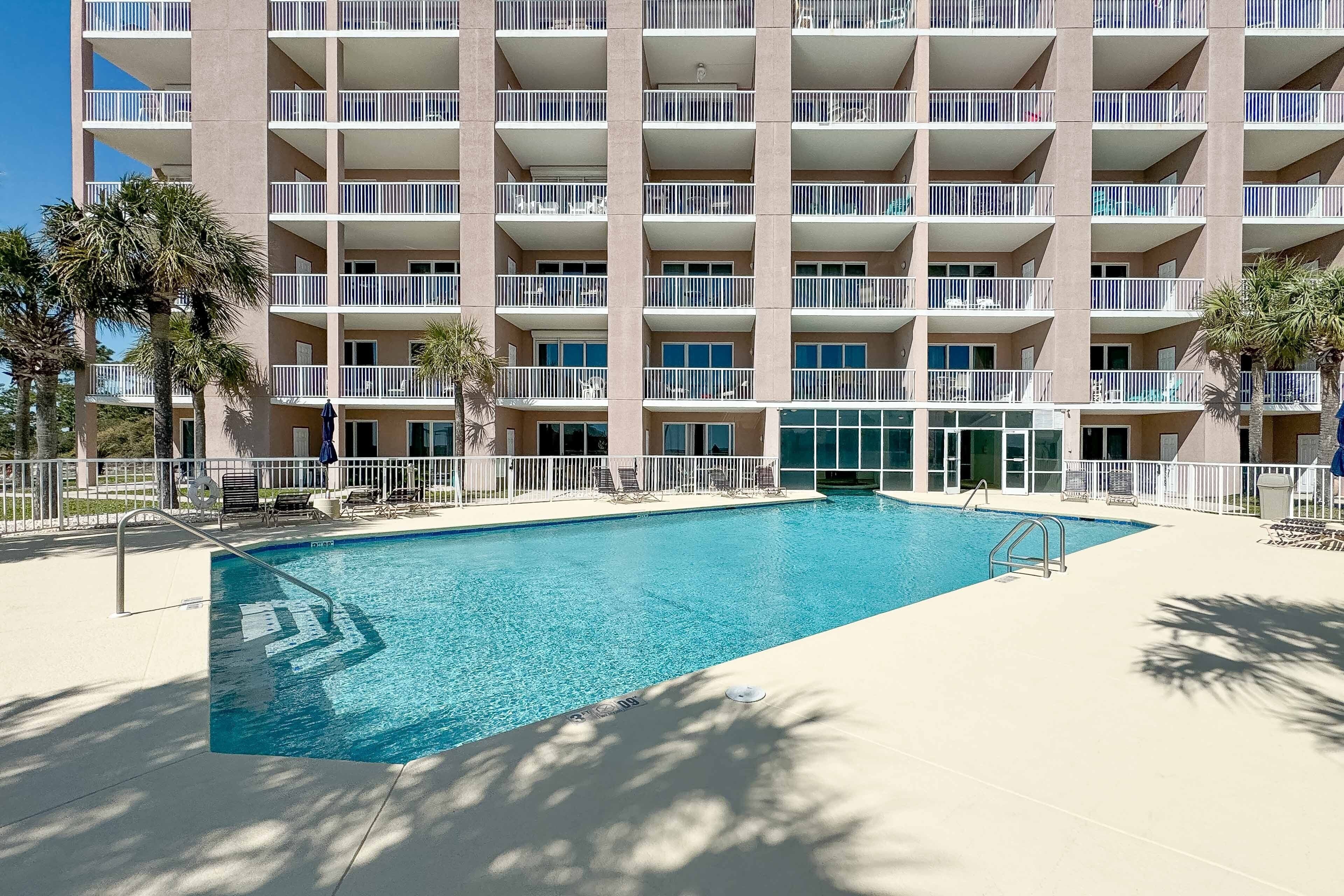 A hotel with a swimming pool, multiple balconies, and palm trees.