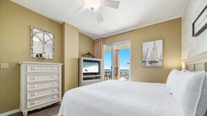 Quarto com uma cama grande, cômoda, televisão e varanda com vista.
