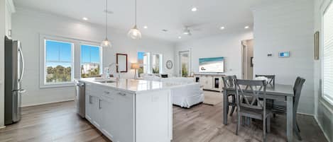 Une cuisine moderne avec des meubles blancs, un îlot central et des luminaires suspendus.