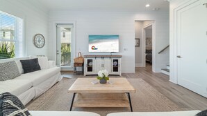 A modern living room with a white sofa, a coffee table with a vase, a television on the wall, and a staircase leading to another room. - PRIVATE HOME WITH BEACH ACCESS AND POOLS! (Gulf Shores)