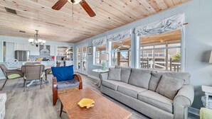 A spacious living area with a wooden ceiling, a sofa, a dining table, and wicker chairs. - COZY LIVING ON THE BEACH! (Gulf Shores)