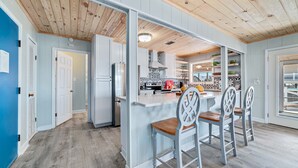 A kitchen with a wooden ceiling, white cabinets, and a central island with bar stools. - COZY LIVING ON THE BEACH! (Gulf Shores)