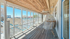 A covered wooden deck with large windows overlooking a pool and buildings. - COZY LIVING ON THE BEACH! (Gulf Shores)