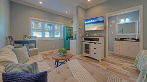 A living room with a sofa, a coffee table, and a TV. There is a kitchen area with cabinets and a refrigerator. - 2 Studio Condos Beach Boardwalk, Pool & Tennis Court Island Retreat Complex (Port Aransas)