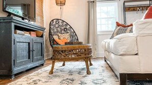 Una sala de estar con un sofá, un sillón de mimbre, un mueble y un televisor.