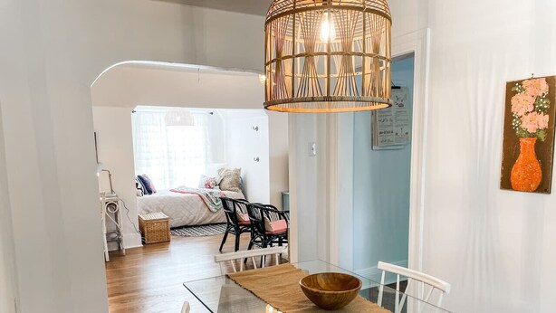 A dining area with a glass table, white chairs, a woven placemat, and a hanging light fixture. - Adorable 1BR Apt. w/ KING bed 1 m. to square! (Columbia)