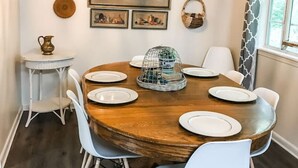 Un comedor con una mesa redonda de madera, sillas blancas y una araña.