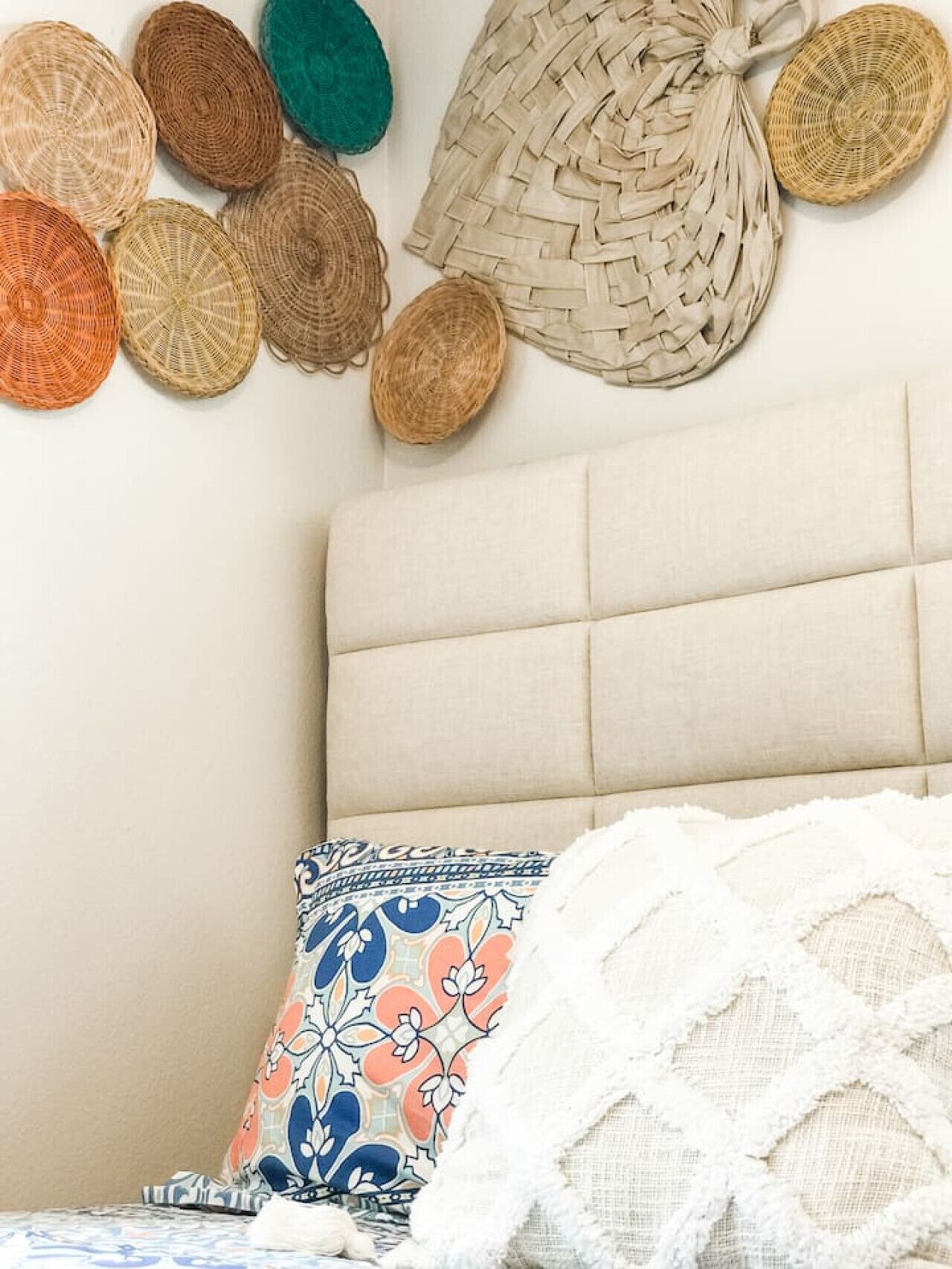 Une chambre à coucher avec une tête de lit recouverte d’un tissu beige, un coussin à motifs et un plaid blanc.