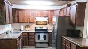 Una cocina moderna con armarios de madera, un refrigerador de acero inoxidable, un microondas y una estufa. Hay un letrero sobre la estufa que dice "Bon Appetit".
