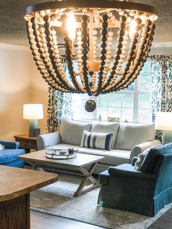Ein Wohnzimmer mit einem modernen Kronleuchter, einem Sofa, einem Couchtisch und einem blauen Sessel.