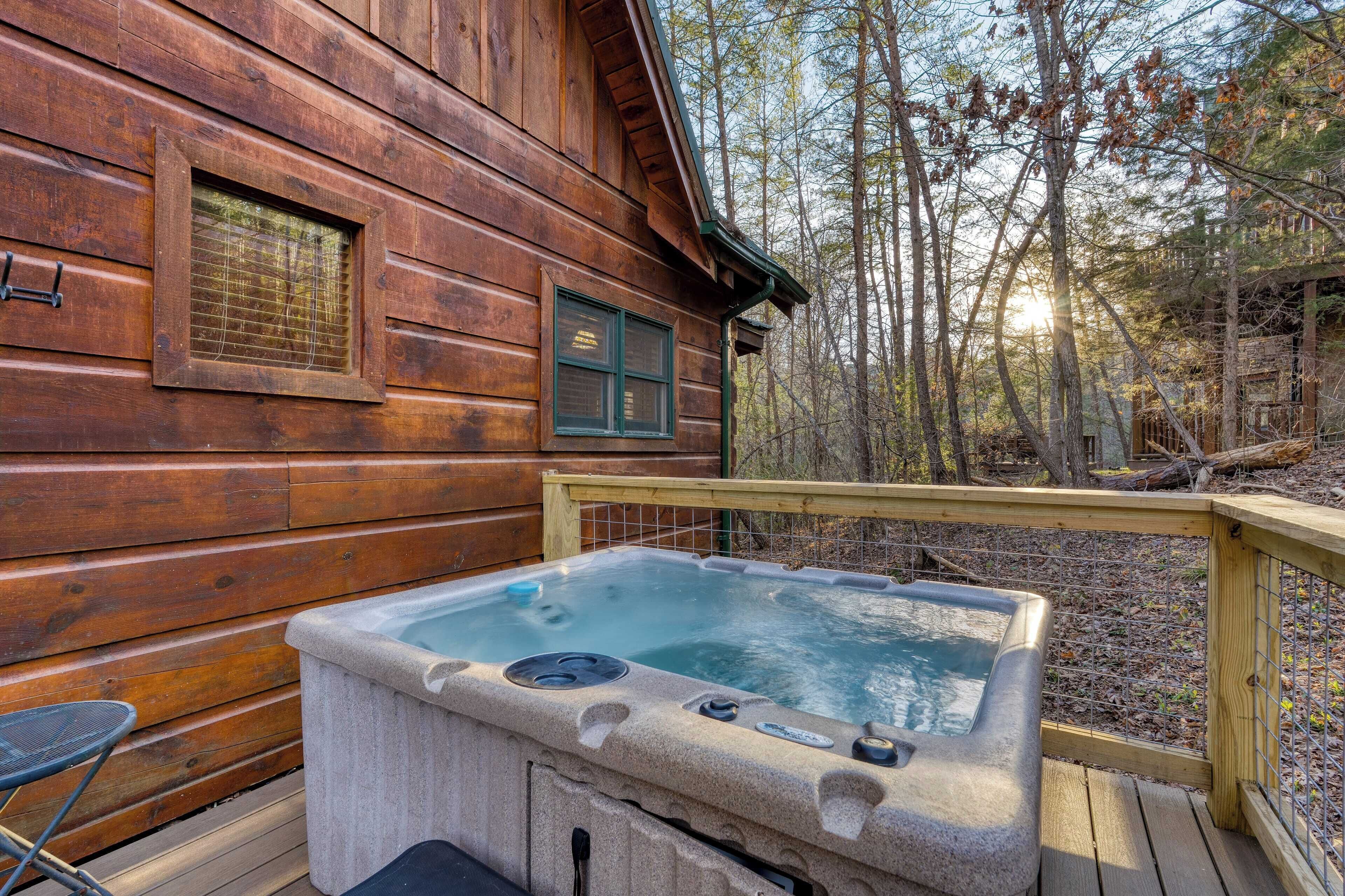 A wooden cabin with a hot tub on a deck, surrounded by trees.