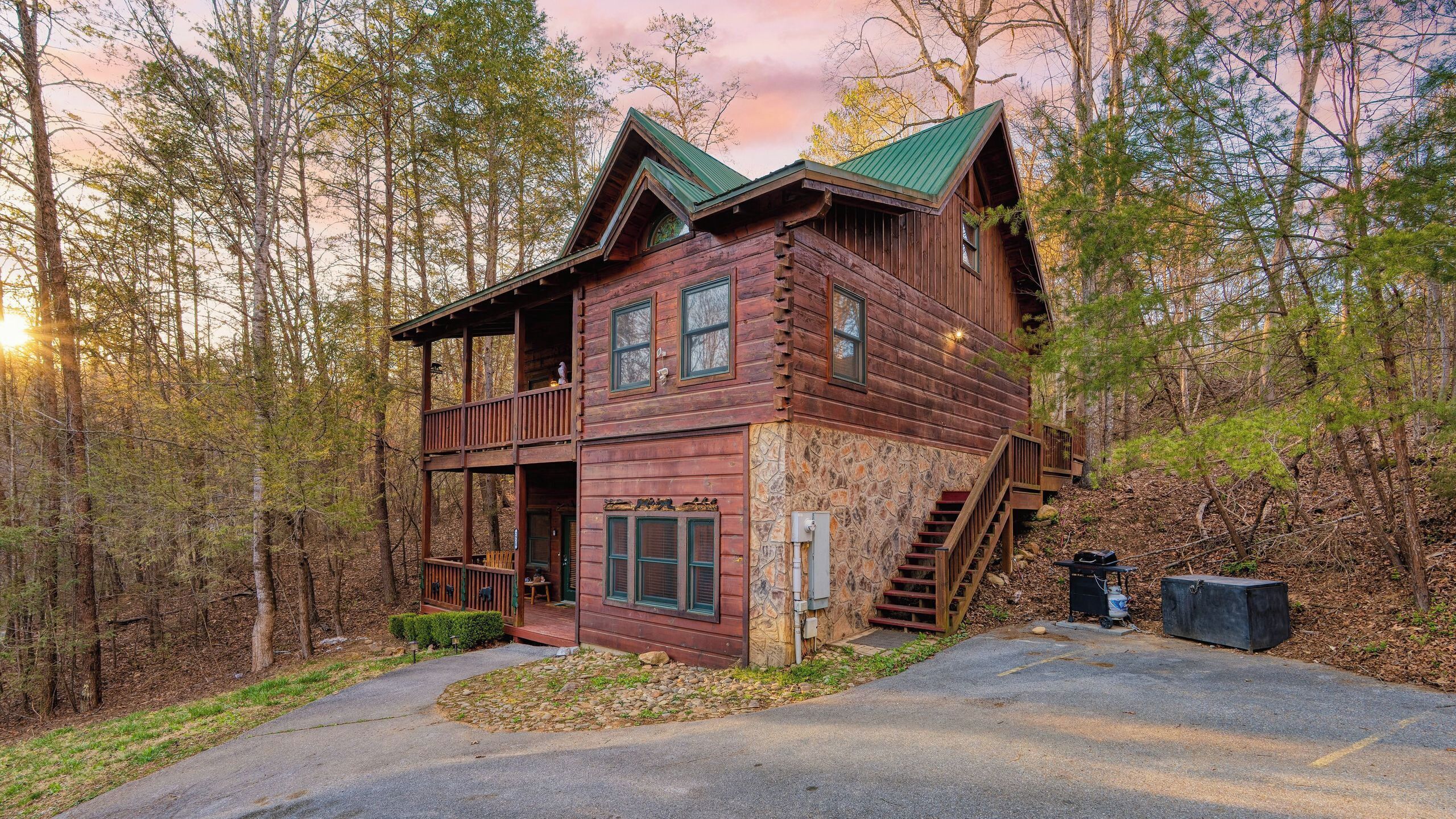 A rustic cabin with a stone foundation, a wooden deck, and a staircase leading to the main entrance.