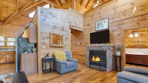 A log cabin interior with a fireplace, a flat-screen TV mounted above it, and a cozy seating area with a sofa and armchair. - Four Bears Lodge by Avantstay Hot Tub, Game Room, Views Near Pigeon Forge (Sevierville)