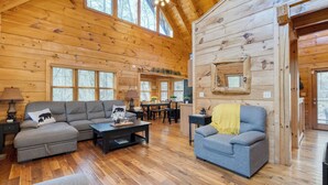 A log cabin interior with a sofa, armchair, dining table, and a fireplace. - Four Bears Lodge by Avantstay Hot Tub, Game Room, Views Near Pigeon Forge (Sevierville)