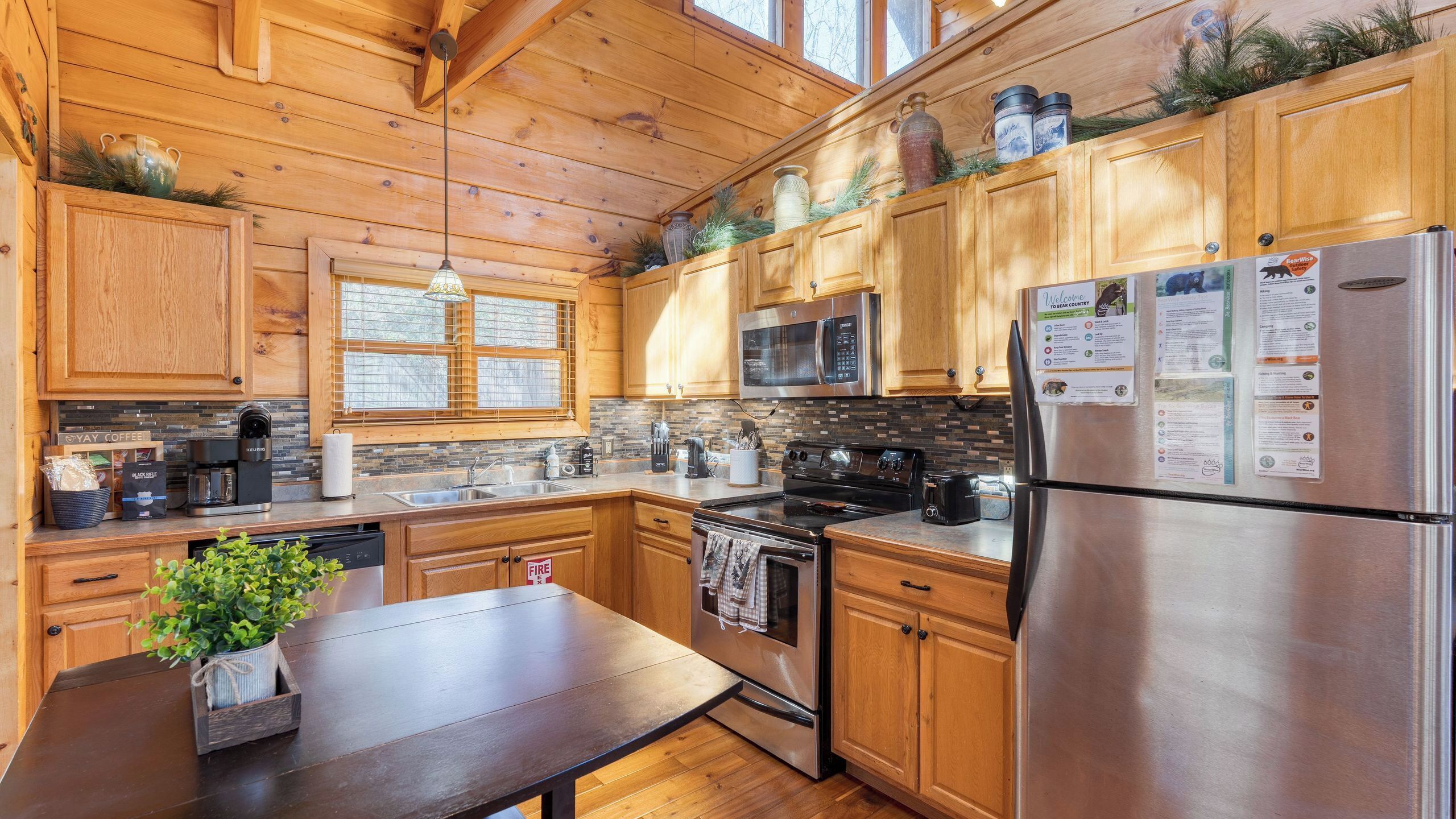 A wooden cabin-style kitchen with a stainless steel refrigerator, a microwave, a stove, and a sink.