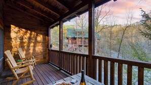 A wooden deck with rocking chairs, a bowl of pretzels, a bottle, and glasses on a table. - Four Bears Lodge by Avantstay Hot Tub, Game Room, Views Near Pigeon Forge (Sevierville)
