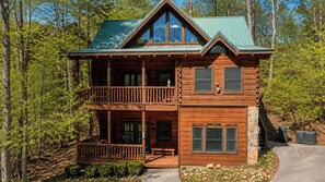 A two-story log cabin with a balcony, a stone foundation, and a metal roof.