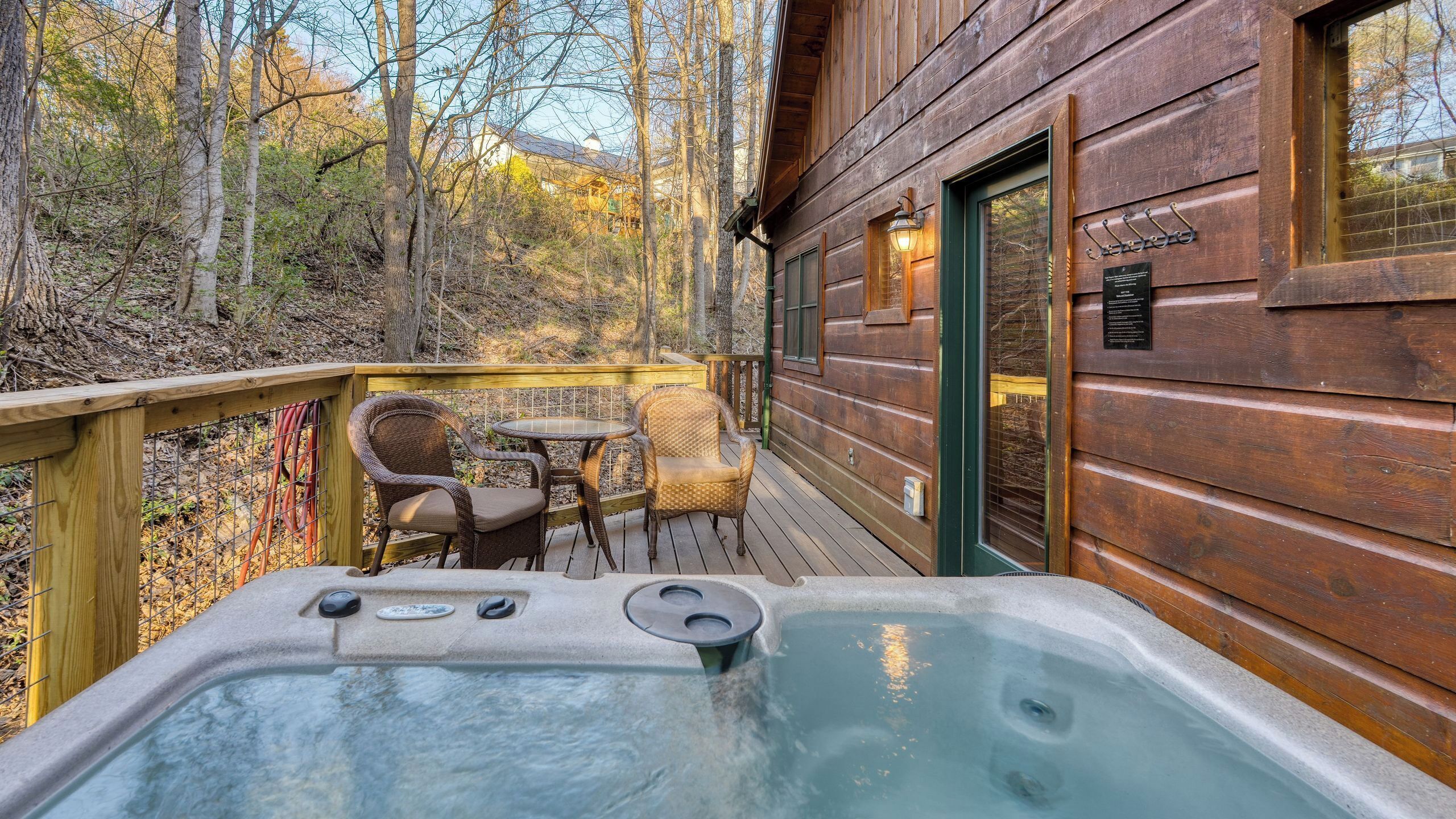 A wooden cabin with a hot tub, outdoor seating, and a view of the forest.