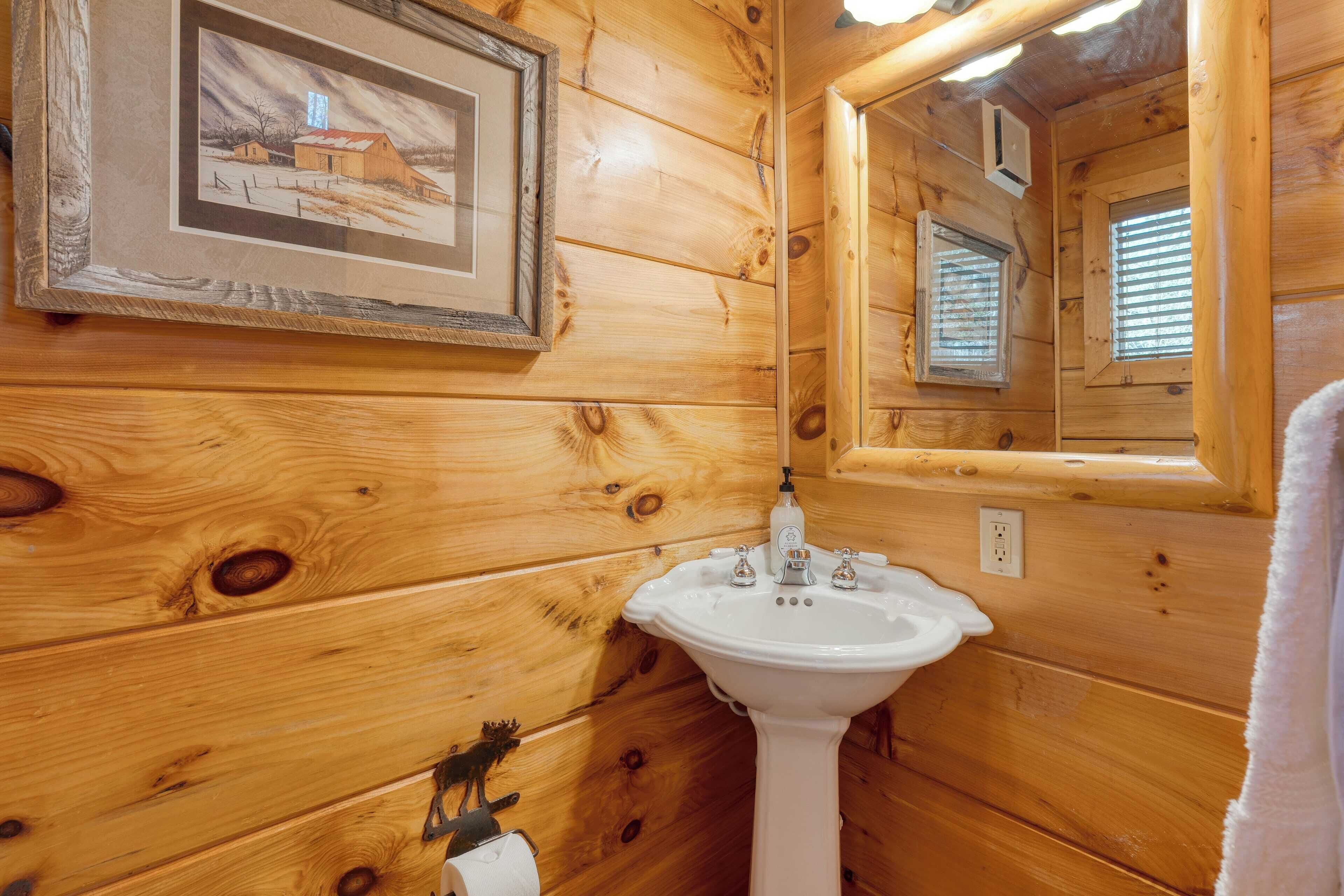 A wooden cabin bathroom with a sink, toilet, and framed picture on the wall.
