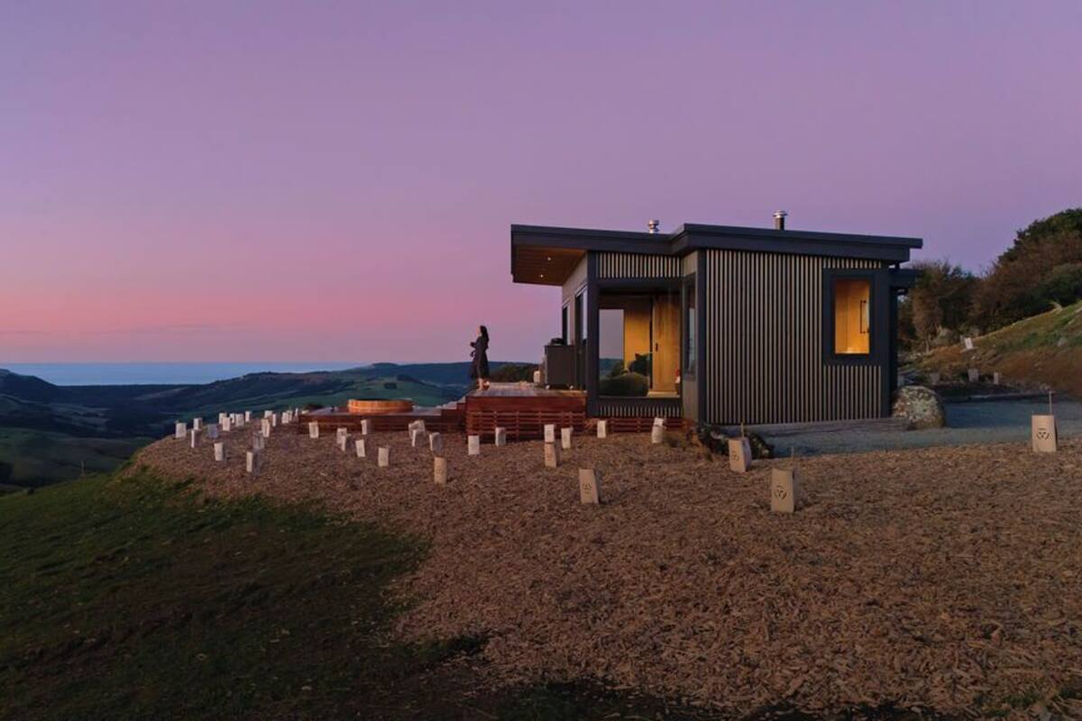 Un edificio moderno con tetto piano, situato su una collina erbosa con vista sul paesaggio circostante.