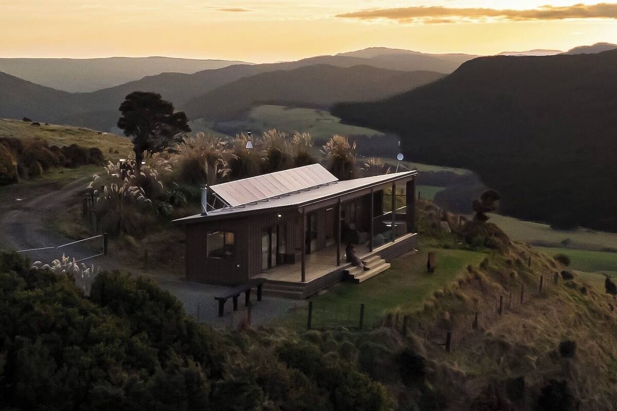 Una casa moderna con tetto piatto, immersa in una proprietà recintata e con vista su dolci colline e una valle.