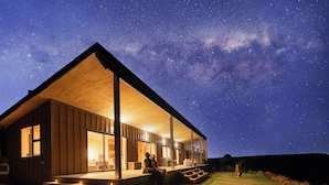 Een modern huis met een ruime open veranda, een houten gevel en uitzicht op de nachthemel.