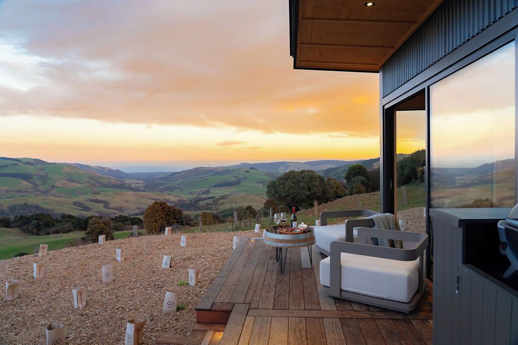An outdoor deck with a fire pit, seating, and a scenic view of rolling hills during sunset.
