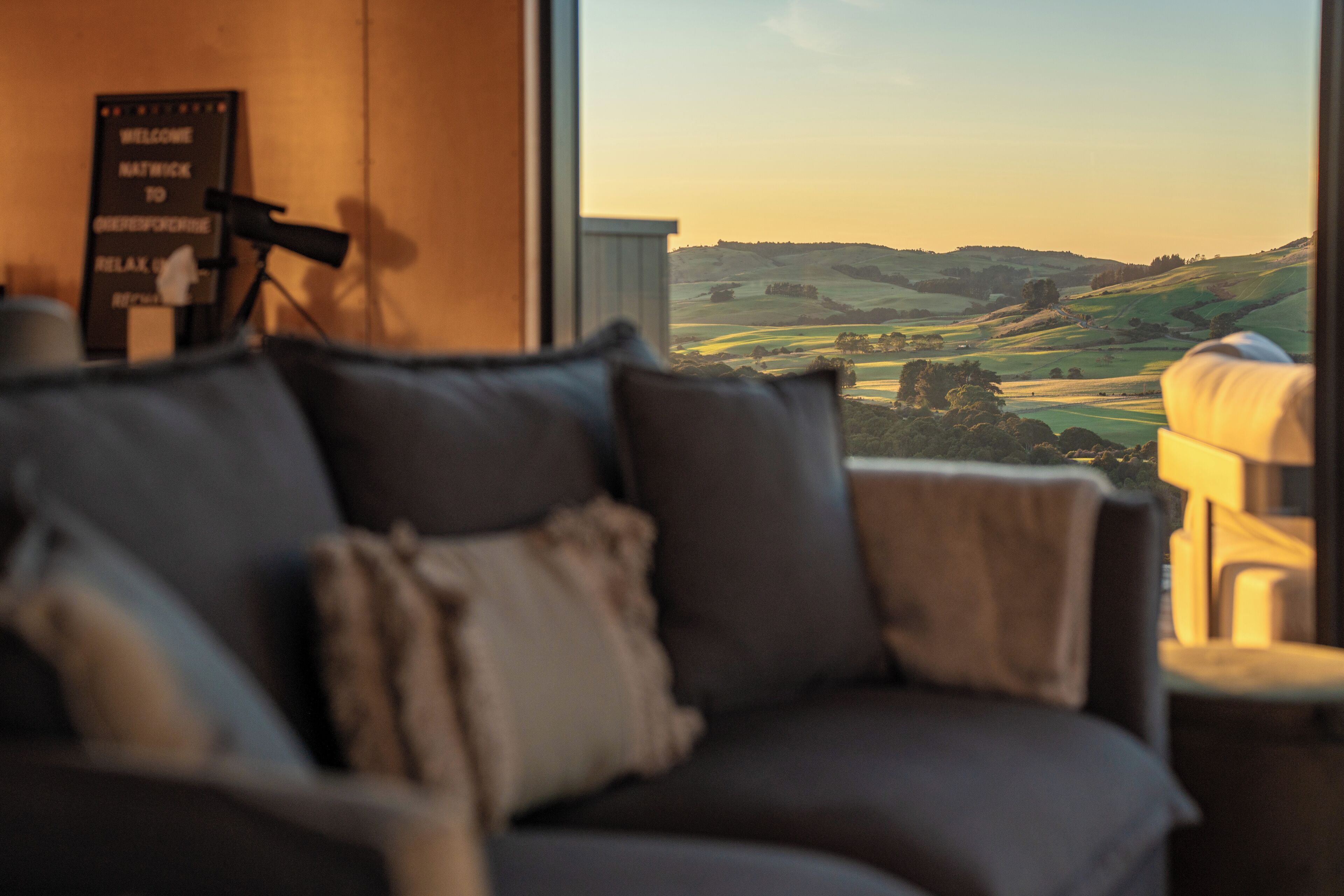 A room with a view of rolling hills, a couch, and a telescope.