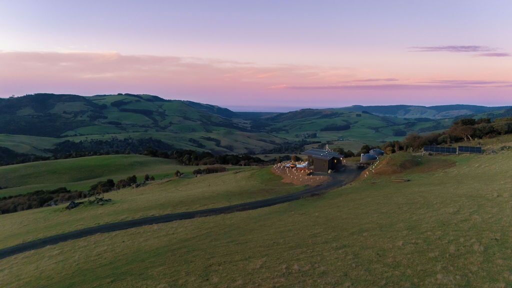 Un paisaje rural con colinas onduladas, una casa de campo y paneles solares.