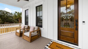 A porch with two wooden chairs, a wooden door with a glass panel, and a ceiling fan. - Newly Built IOP Home – Pool, Ping Pong, Walk to Beach, Shops & Restaurants (Isle Of Palms)