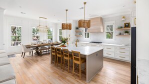 A spacious kitchen with a large island, wooden chairs, and pendant lighting. - Newly Built IOP Home – Pool, Ping Pong, Walk to Beach, Shops & Restaurants (Isle Of Palms)