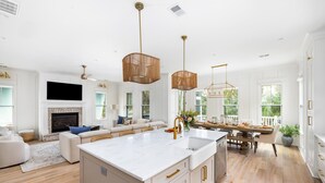 A spacious kitchen with a large island, white cabinetry, and a dining area with a wooden table and chairs. - Newly Built IOP Home – Pool, Ping Pong, Walk to Beach, Shops & Restaurants (Isle Of Palms)