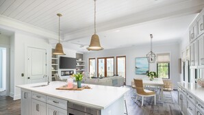 A spacious kitchen with a large island, white cabinetry, and pendant lighting.